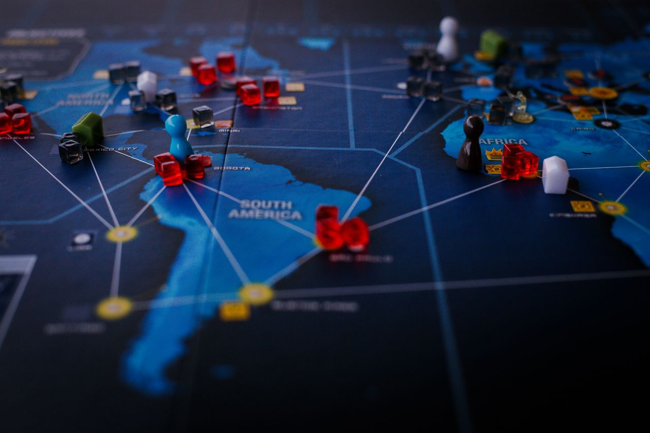 hero-img-02 A strategic board game featuring a world map and colorful playing pieces.
