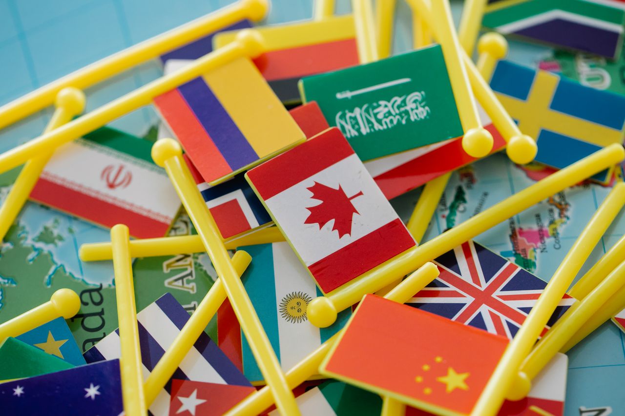 hero-img-01 Colorful mini flags of countries on a world map, symbolizing global connections.